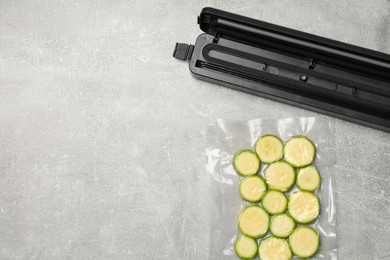 Photo of Vacuum packing sealer with plastic bag of zucchini on light grey table, flat lay. Space for text