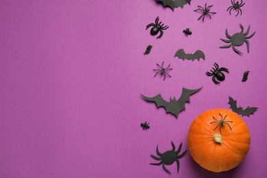 Flat lay composition with pumpkin, spiders and paper bats on purple background, space for text. Halloween celebration