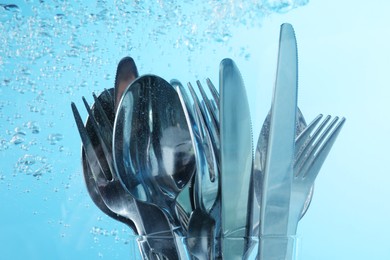 Photo of Washing silver cutlery in water on light blue background