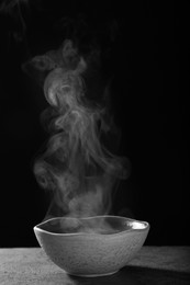 Photo of Bowl with steam on table against black background