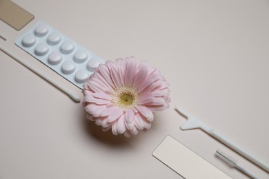 Sterile gynecological tools, pills and gerbera flower on beige background, above view