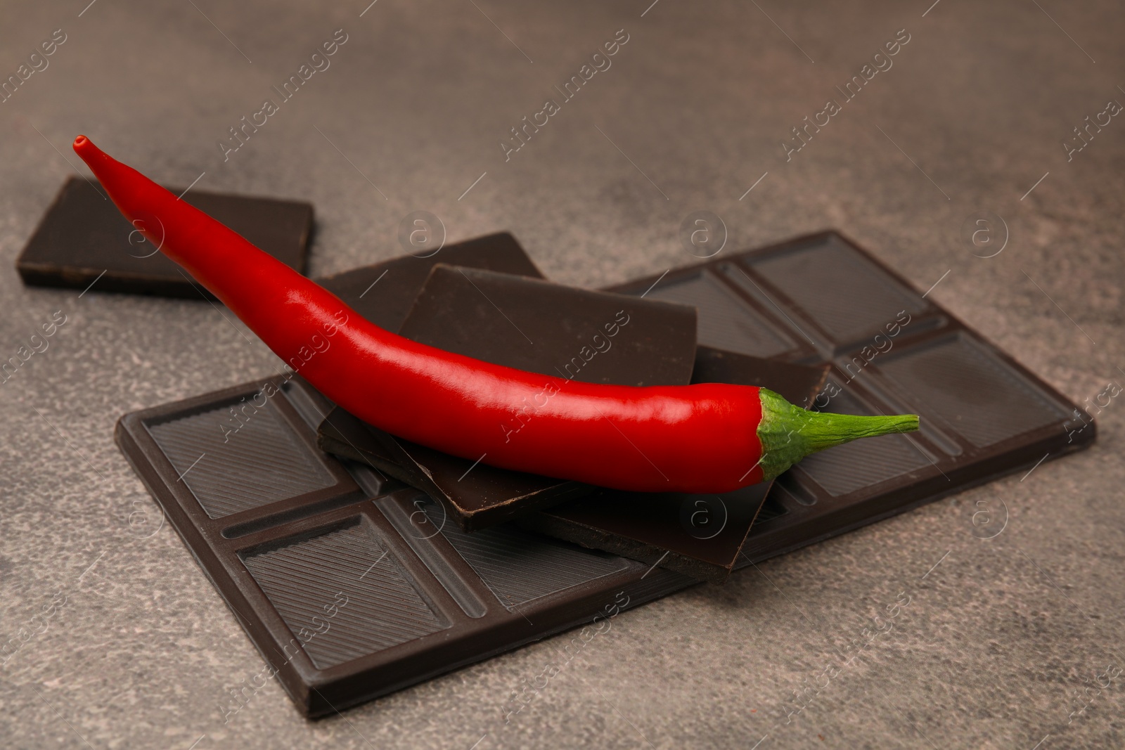 Photo of Delicious chocolate and fresh red chili pepper on grey textured table