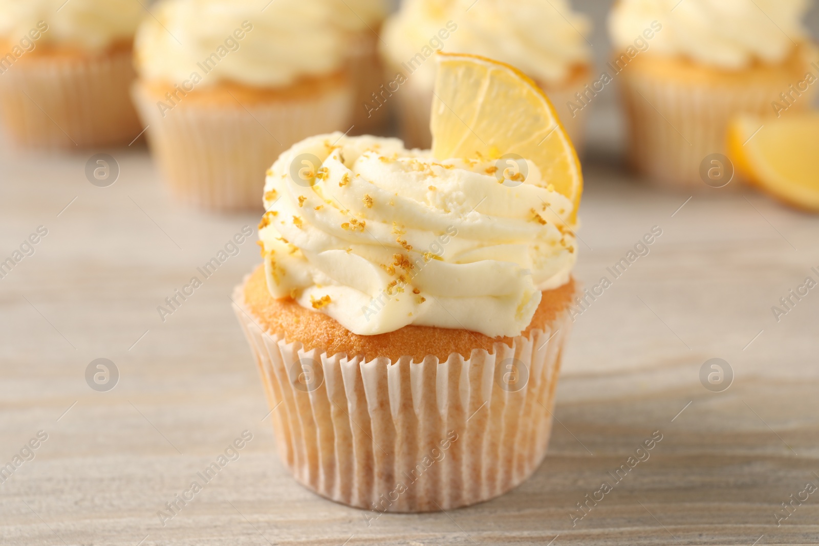 Photo of Tasty cupcake with cream, zest and lemon slice on light wooden table, closeup