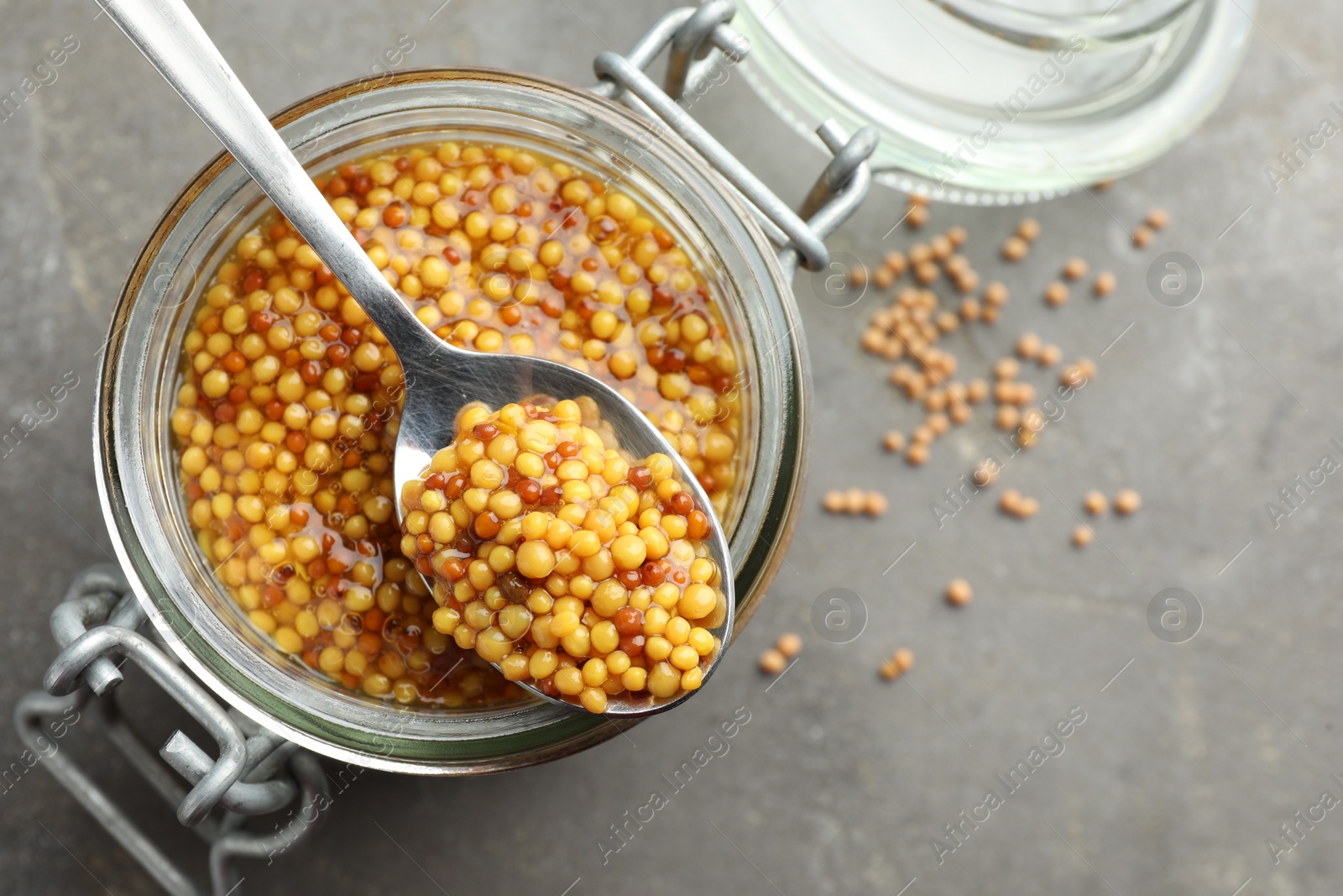 Photo of Whole grain mustard in jar and spoon on grey table, top view. Space for text