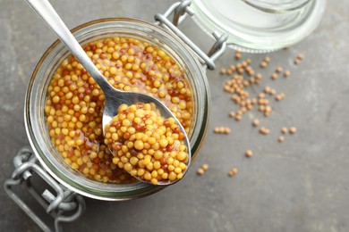 Photo of Whole grain mustard in jar and spoon on grey table, top view. Space for text