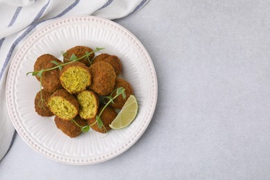 Photo of Delicious falafel balls, lime slice and microgreens on light table, top view. Space for text