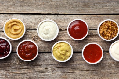 Different tasty sauces in bowls on wooden table, flat lay
