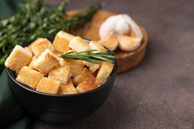 Photo of Delicious crispy croutons in bowl and rosemary on dark table, closeup. Space for text