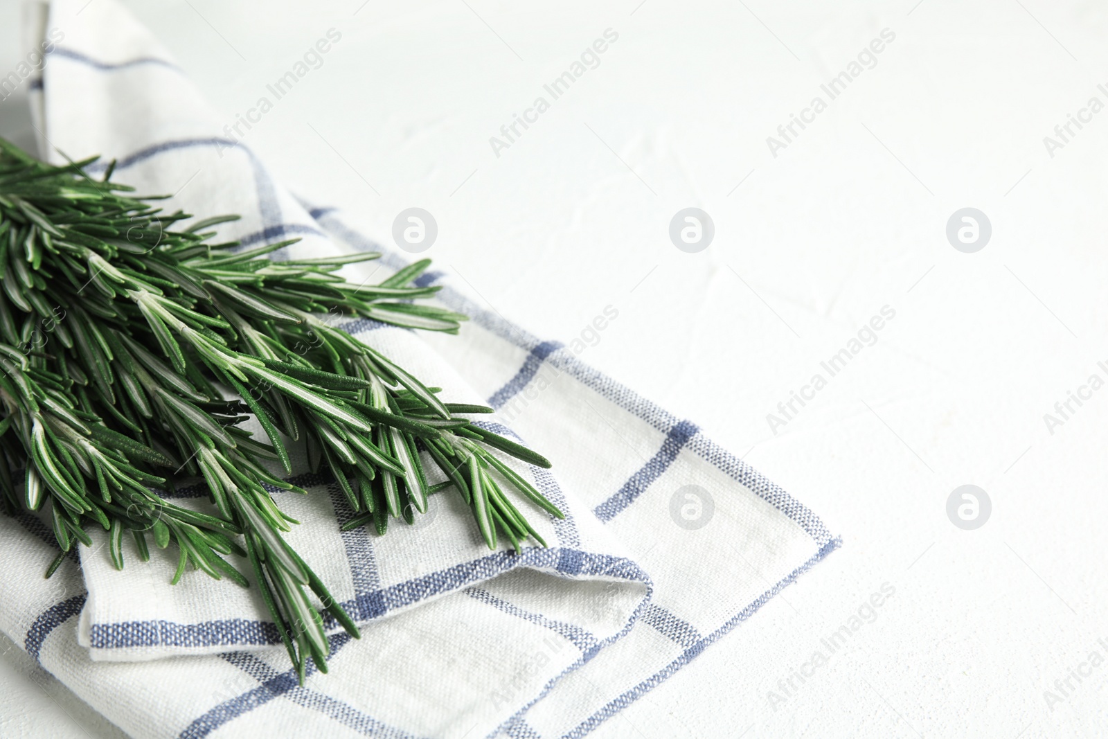 Photo of Fresh green rosemary and napkin on white table. Space for text