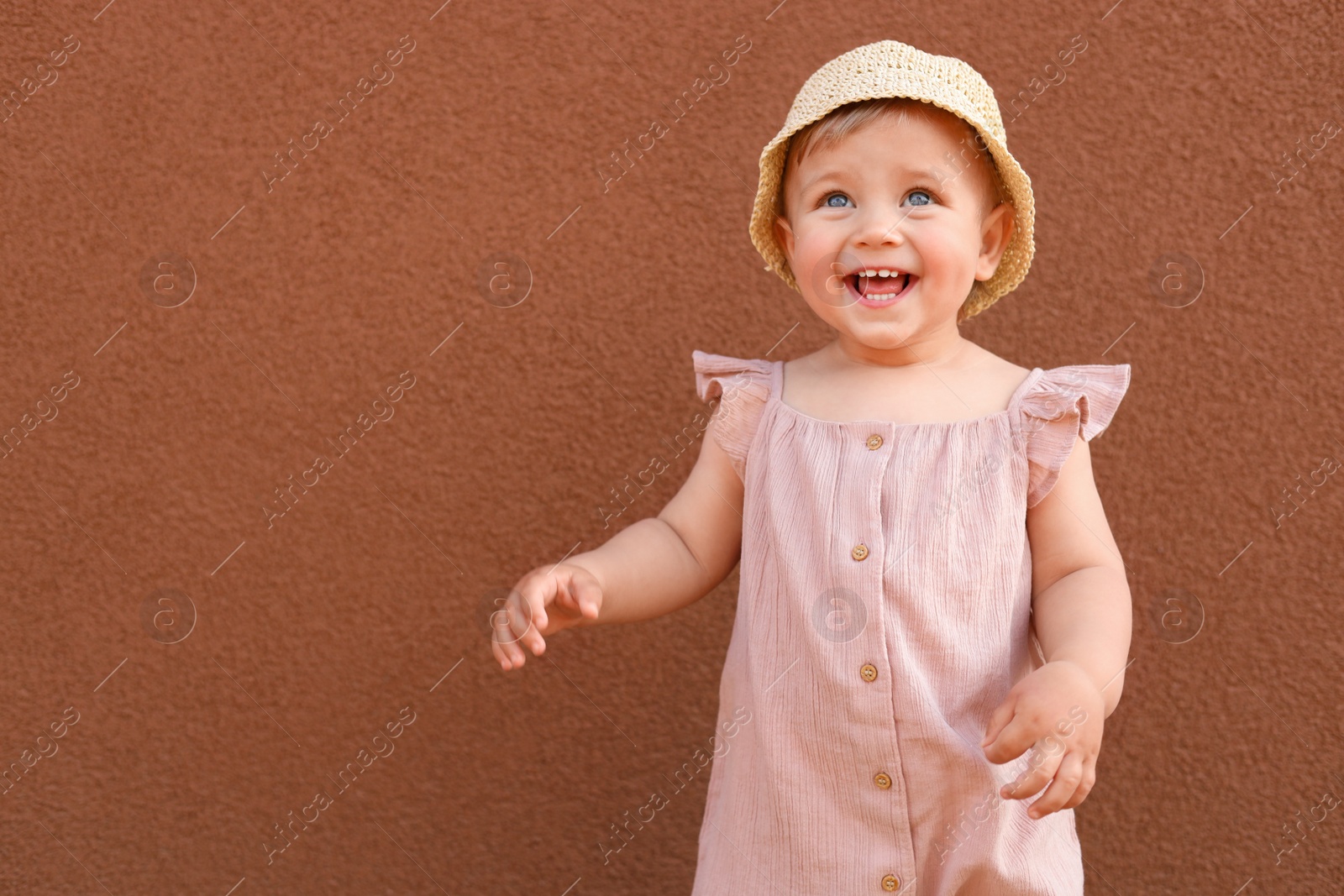 Photo of Cute little girl wearing stylish clothes near brown wall. Space for text