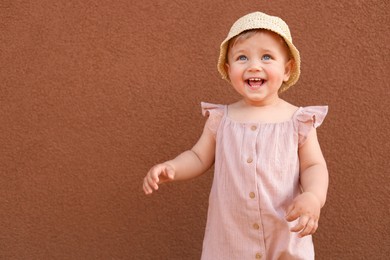 Photo of Cute little girl wearing stylish clothes near brown wall. Space for text