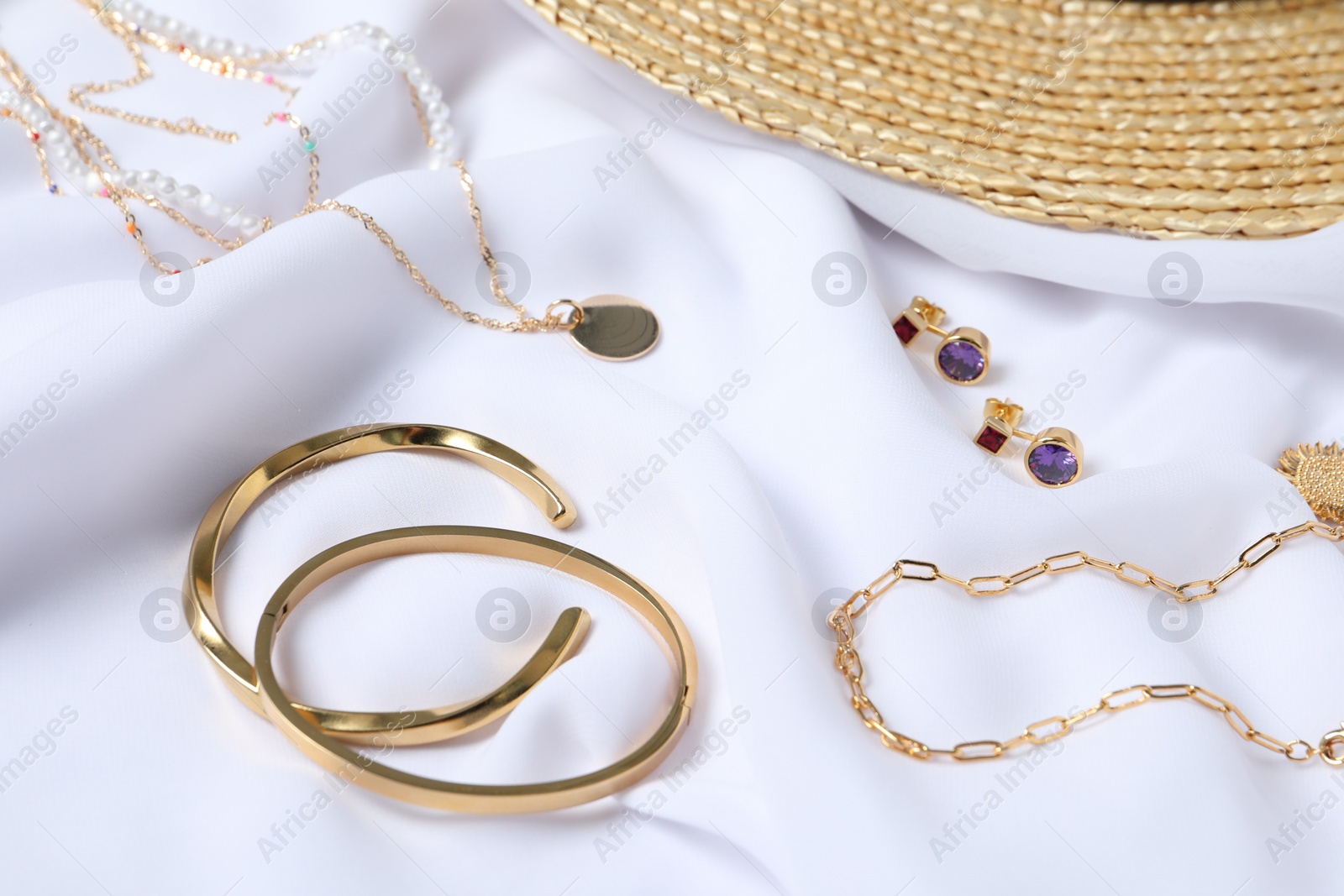 Photo of Elegant bracelets, necklaces and earrings on white cloth