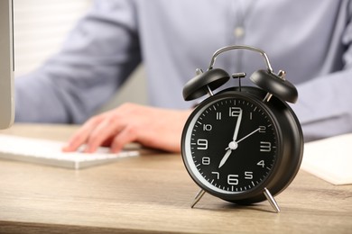Photo of Black alarm clock and man working at wooden table, closeup. Space for text