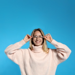 Beautiful young woman wearing knitted sweater on light blue background