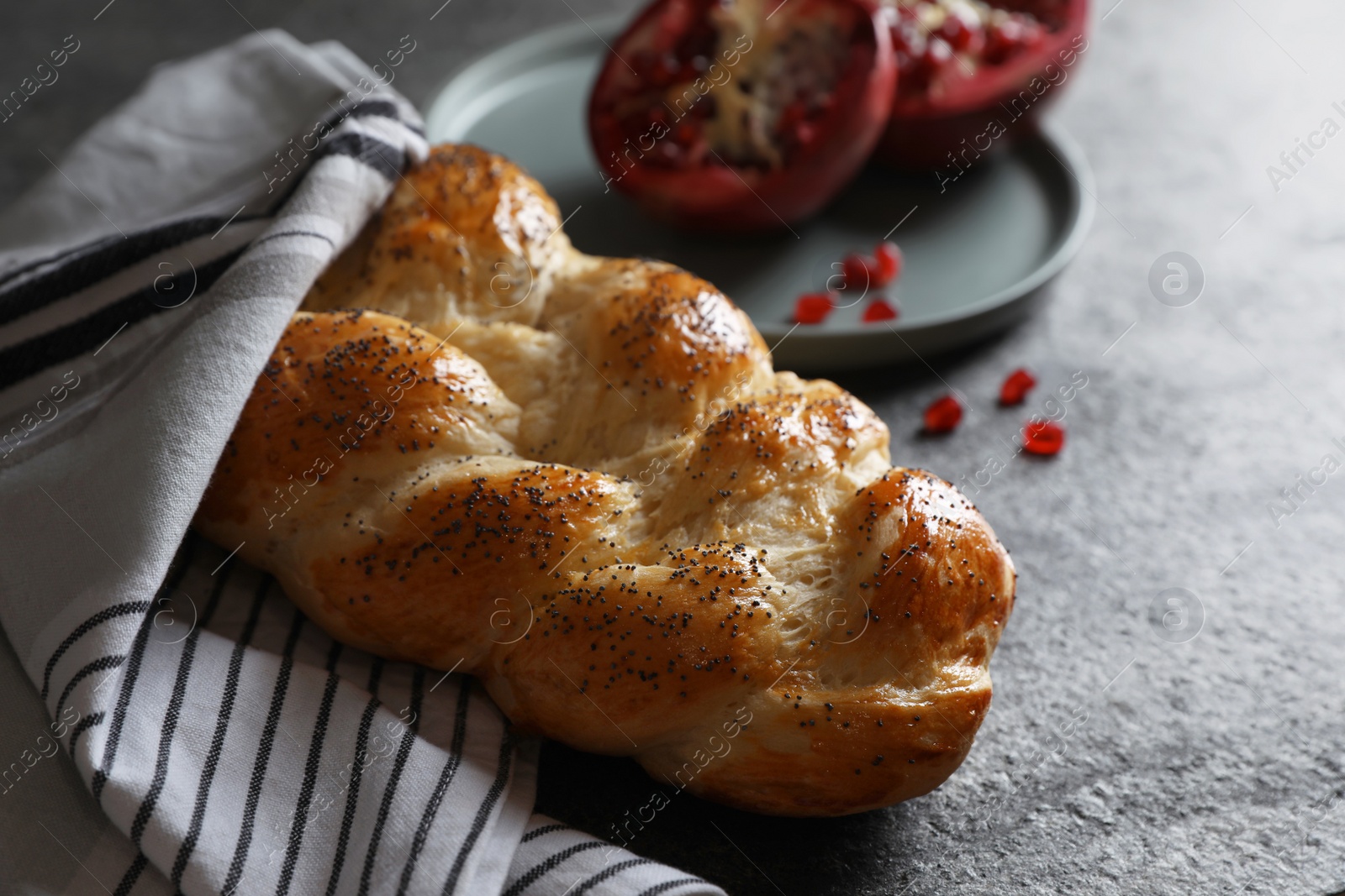 Photo of Homemade braided bread and pomegranate on grey table. Cooking traditional Shabbat challah