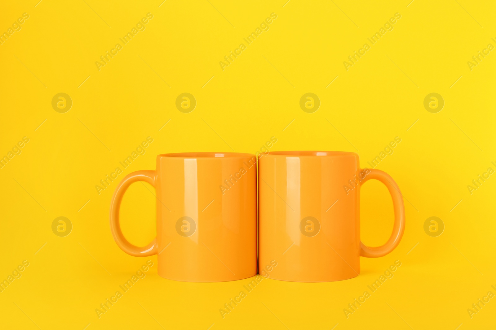 Two blank ceramic mugs on yellow background Photo of Two blank ceramic mugs on yellow background