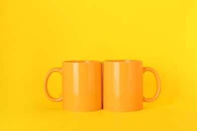 Photo of Two blank ceramic mugs on yellow background