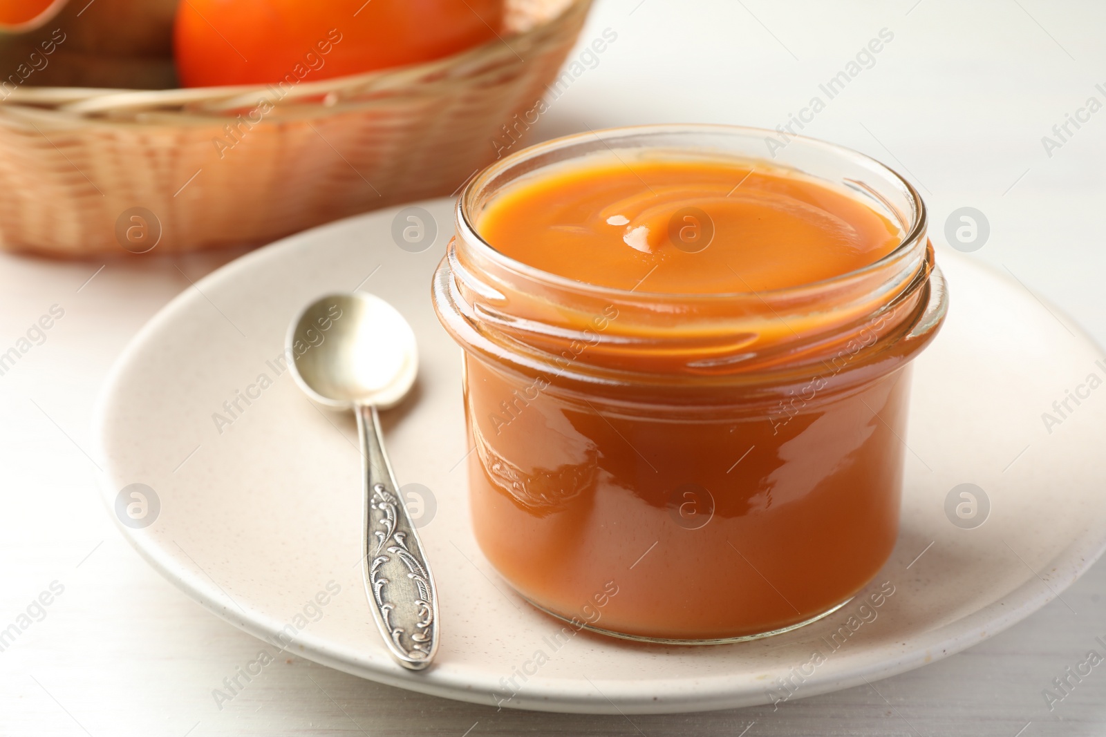 Photo of Delicious persimmon jam in glass jar served on white wooden table, closeup