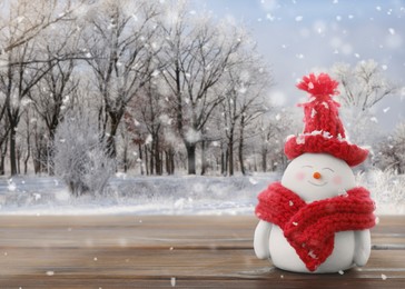 Image of Cute decorative snowman in red hat and scarf on wooden table outdoors, space for text