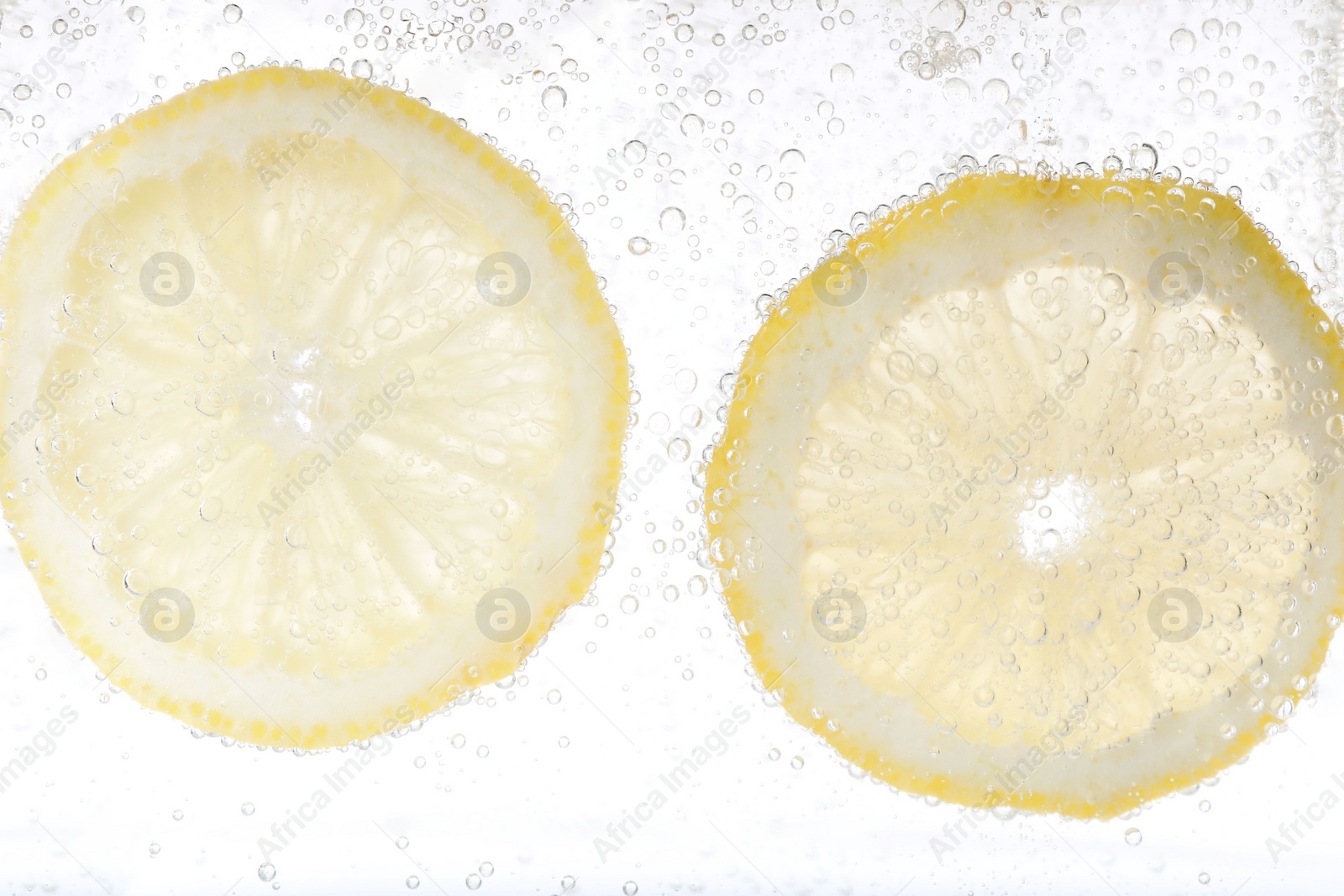 Photo of Juicy lemon slices in soda water against white background, closeup