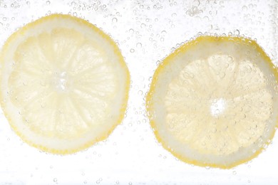 Photo of Juicy lemon slices in soda water against white background, closeup