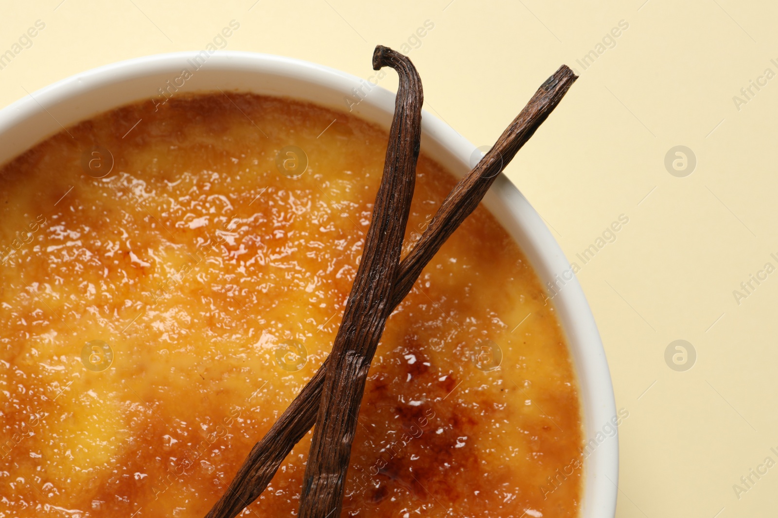 Photo of Delicious creme brulee with vanilla sticks on beige background, top view