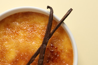 Delicious creme brulee with vanilla sticks on beige background, top view