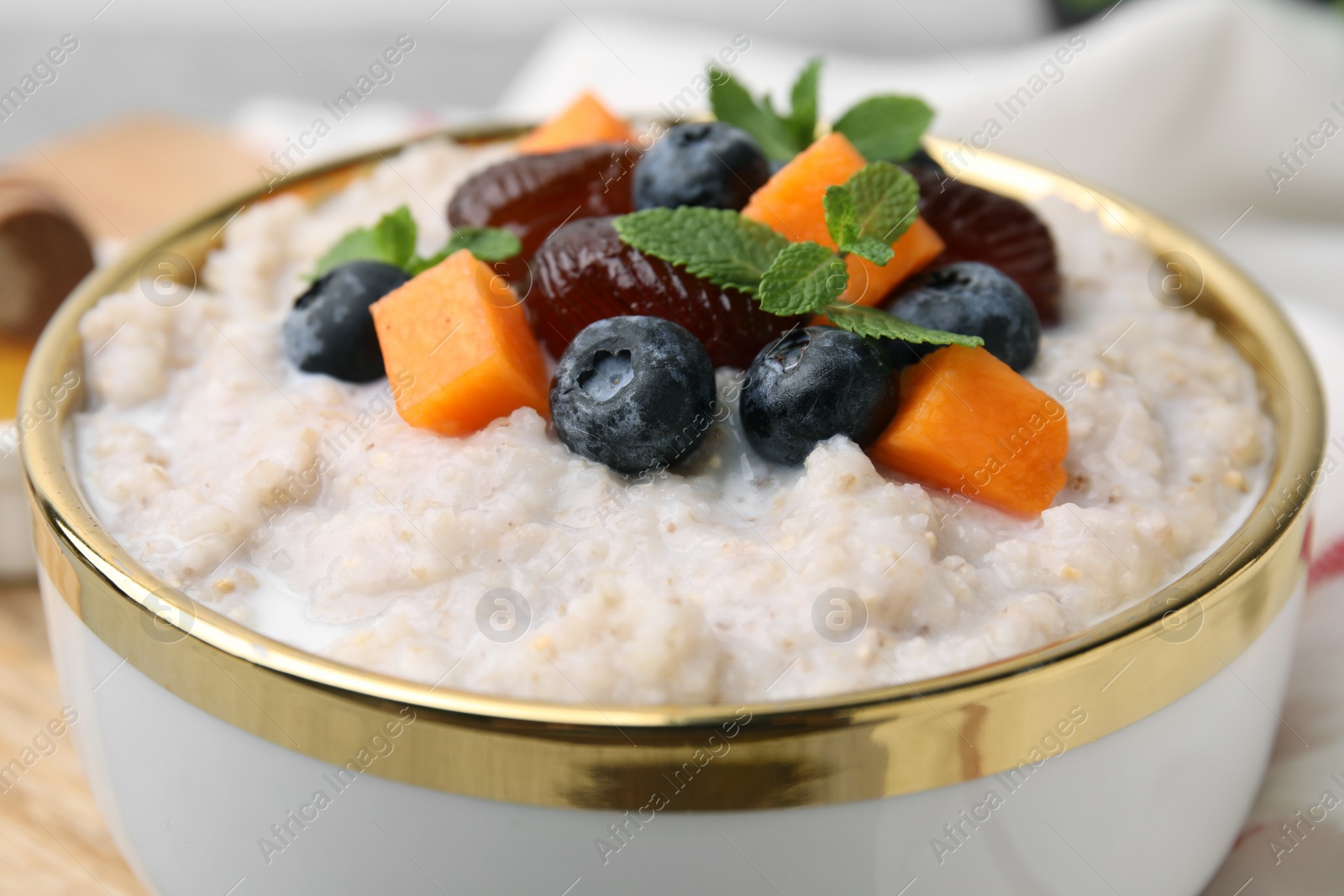 Photo of Delicious barley porridge with blueberries, pumpkin, dates and mint in bowl on table, closeup