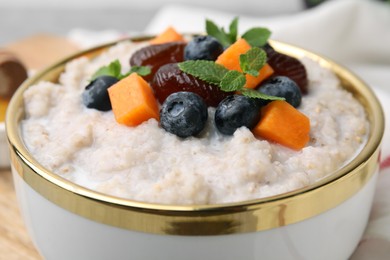 Delicious barley porridge with blueberries, pumpkin, dates and mint in bowl on table, closeup