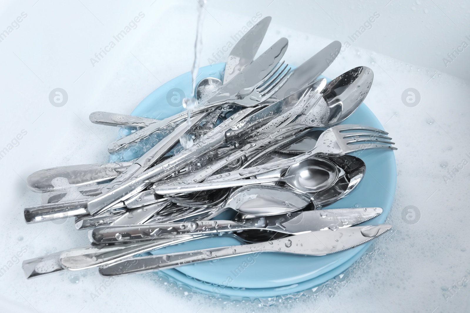 Photo of Washing silver spoons, forks and knives under stream of water in kitchen sink, above view