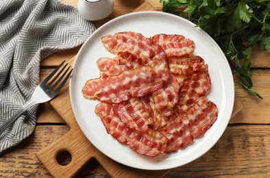 Photo of Fried bacon slices served on wooden table, flat lay