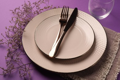Photo of Stylish table setting. Plates, cutlery and floral decor on purple background