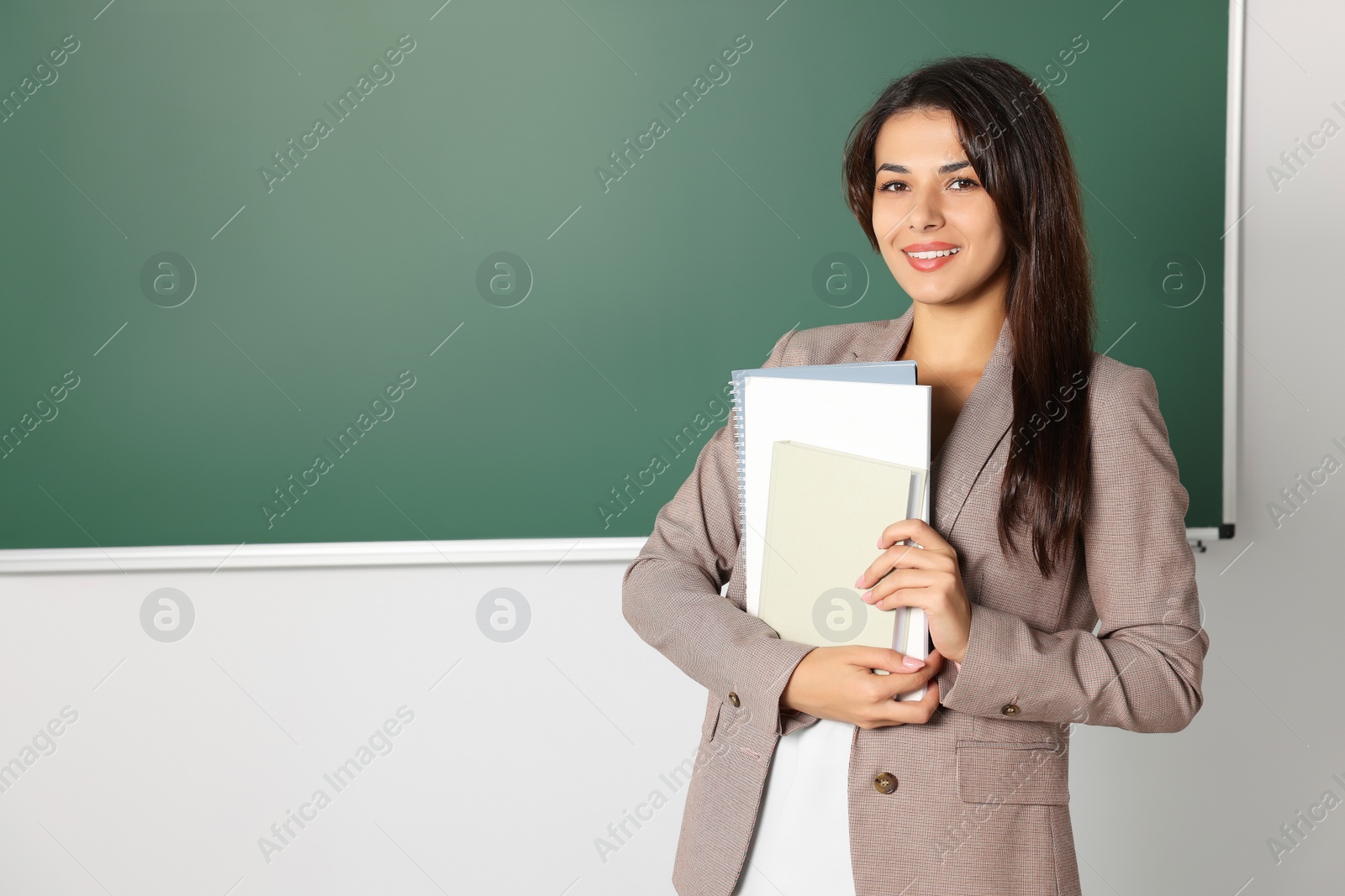 Photo of Happy young teacher giving lesson at blackboard in classroom. Space for text