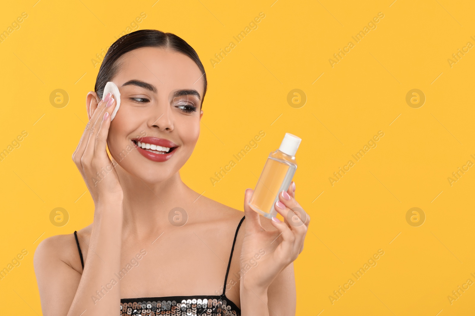 Photo of Beautiful woman removing makeup with cotton pad on orange background, space for text