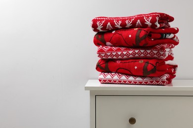 Different folded Christmas sweaters on chest of drawers against light background. Space for text
