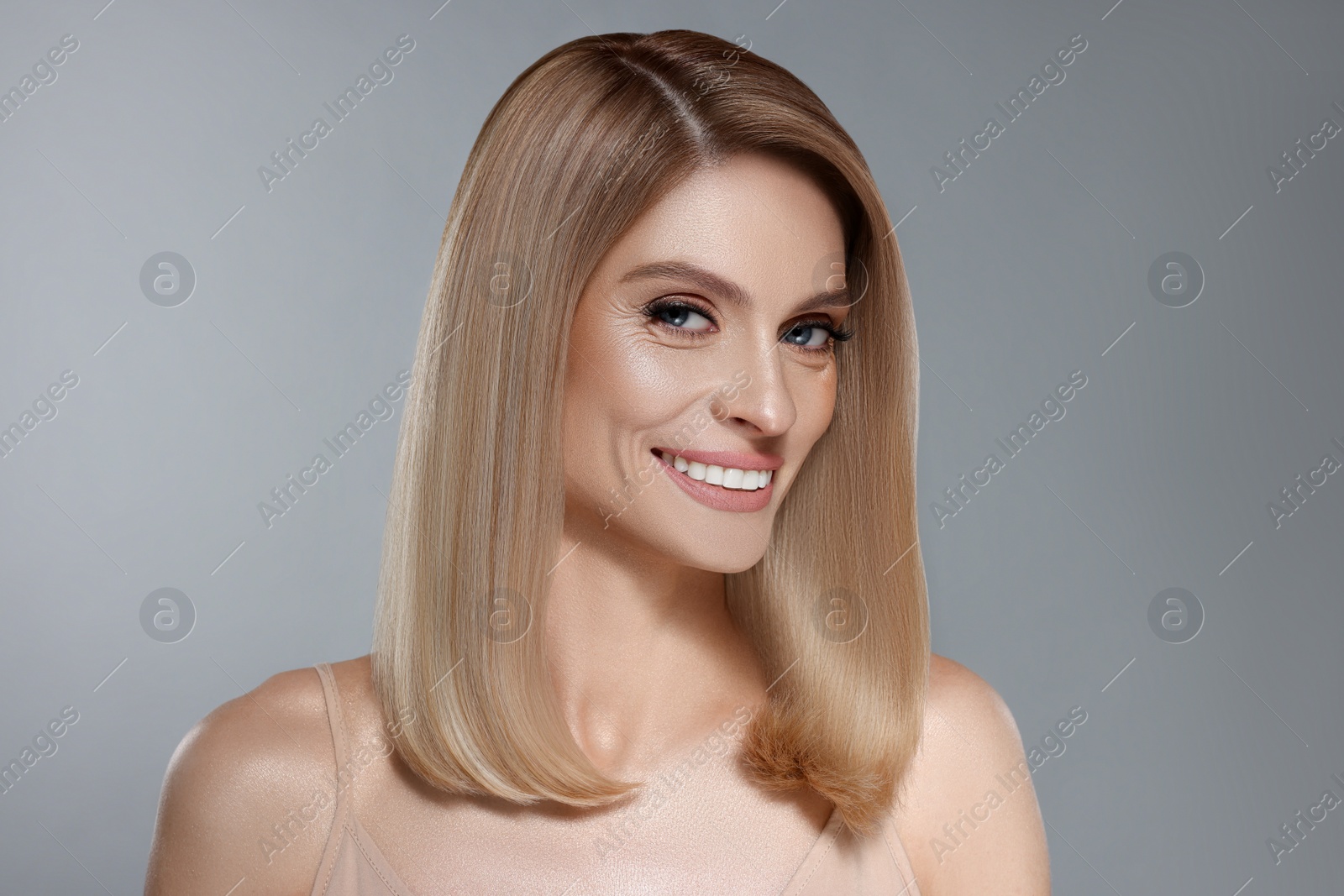 Image of Portrait of attractive woman with blonde hair smiling on grey background