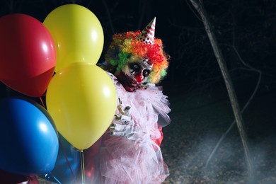 Photo of Terrifying clown with air balloons outdoors at night. Halloween party costume