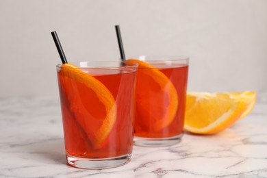 Aperol spritz cocktail, orange slices and straws in glasses on white marble table