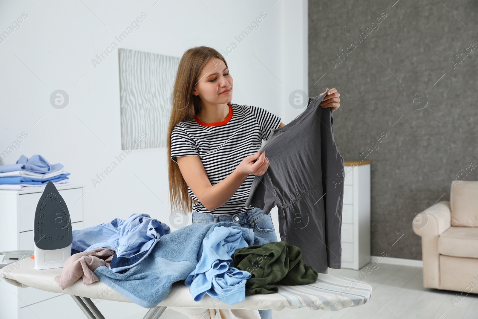 Photo of Young woman with clothes near ironing board at home