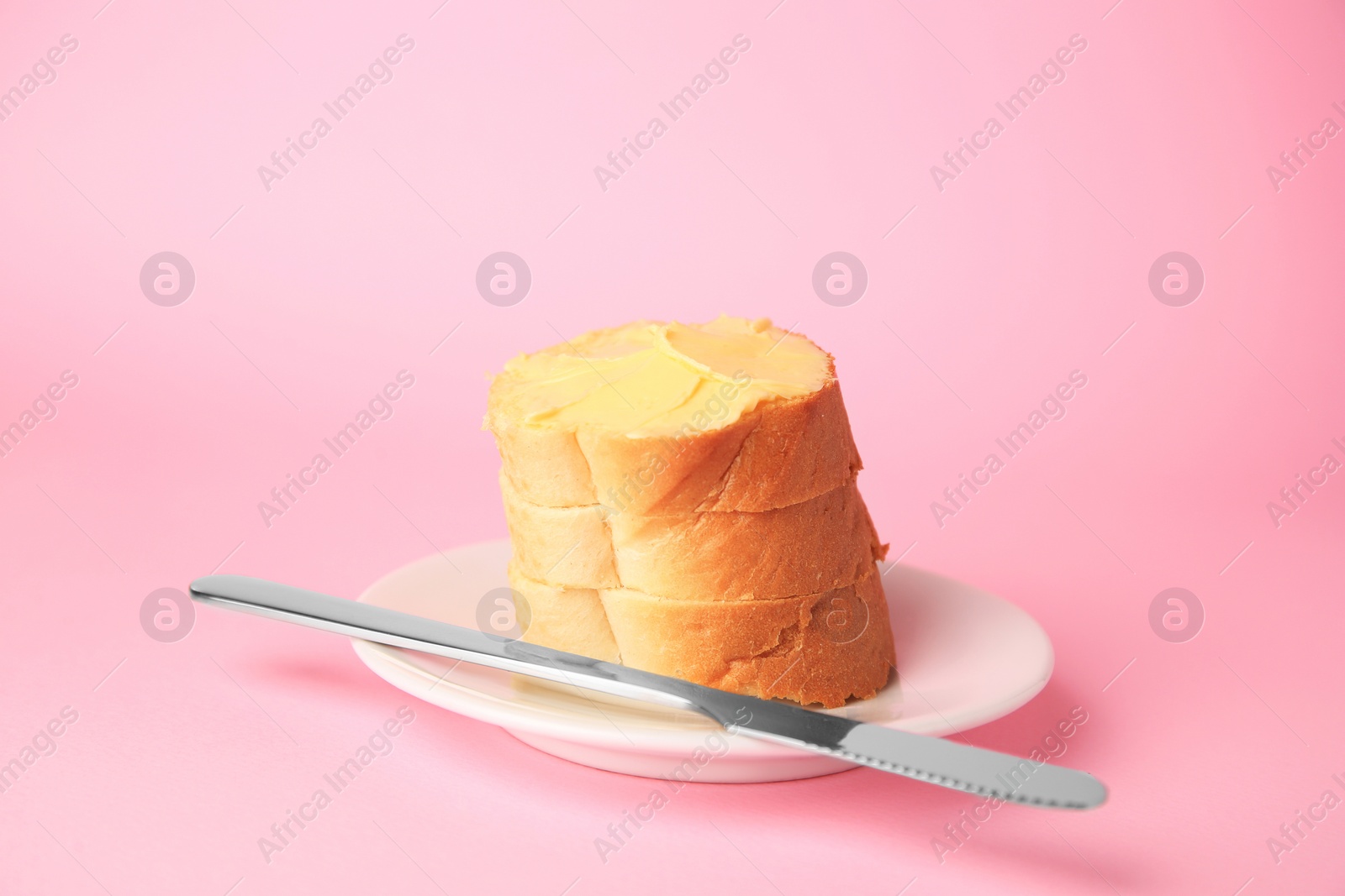 Photo of Slices of delicious baguette with butter and knife on pale pink background