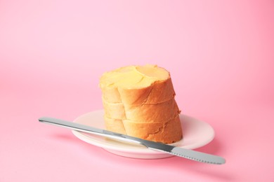 Slices of delicious baguette with butter and knife on pale pink background