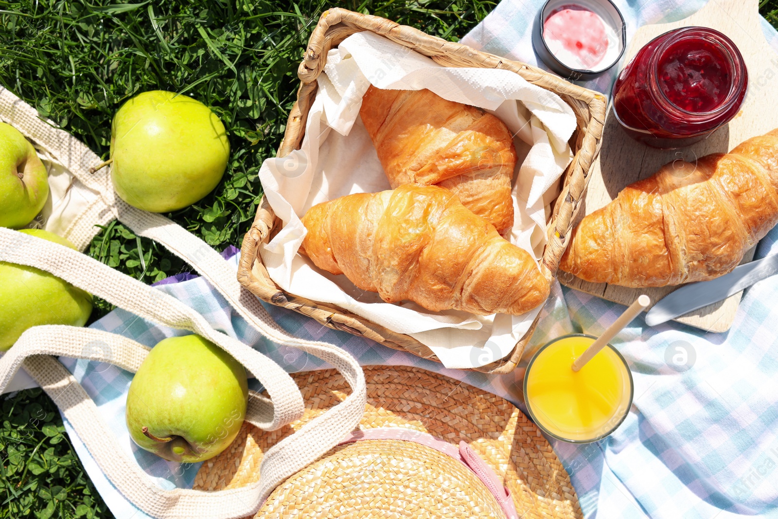 Photo of Blanket with juice, jam and croissants for picnic on green grass, flat lay