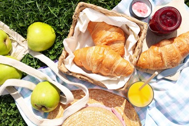 Blanket with juice, jam and croissants for picnic on green grass, flat lay