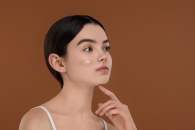 Photo of Teenage girl with swatch of foundation on face against brown background. Space for text