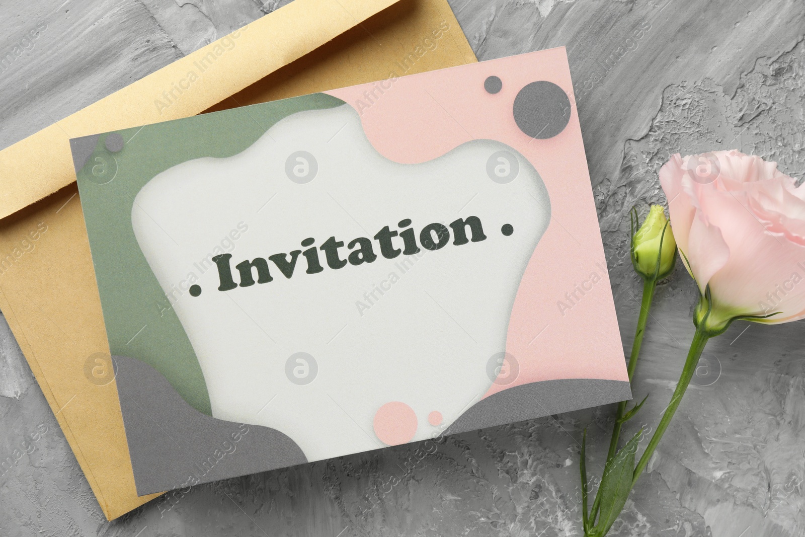 Photo of Beautiful card with word Invitation, envelope and pink flower on grey table, flat lay