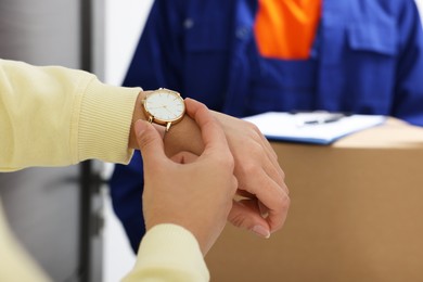 Photo of Closeup view of woman checking time near courier with parcel