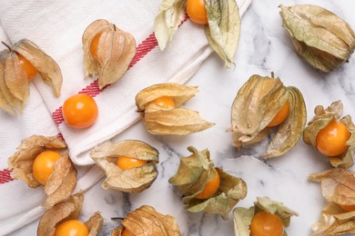 Ripe physalis fruits with dry husk on white marble table, flat lay