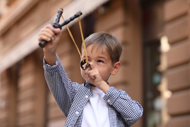 Photo of Little boy playing with slingshot outdoors on city street