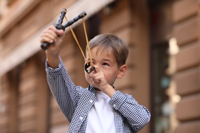 Little boy playing with slingshot outdoors on city street