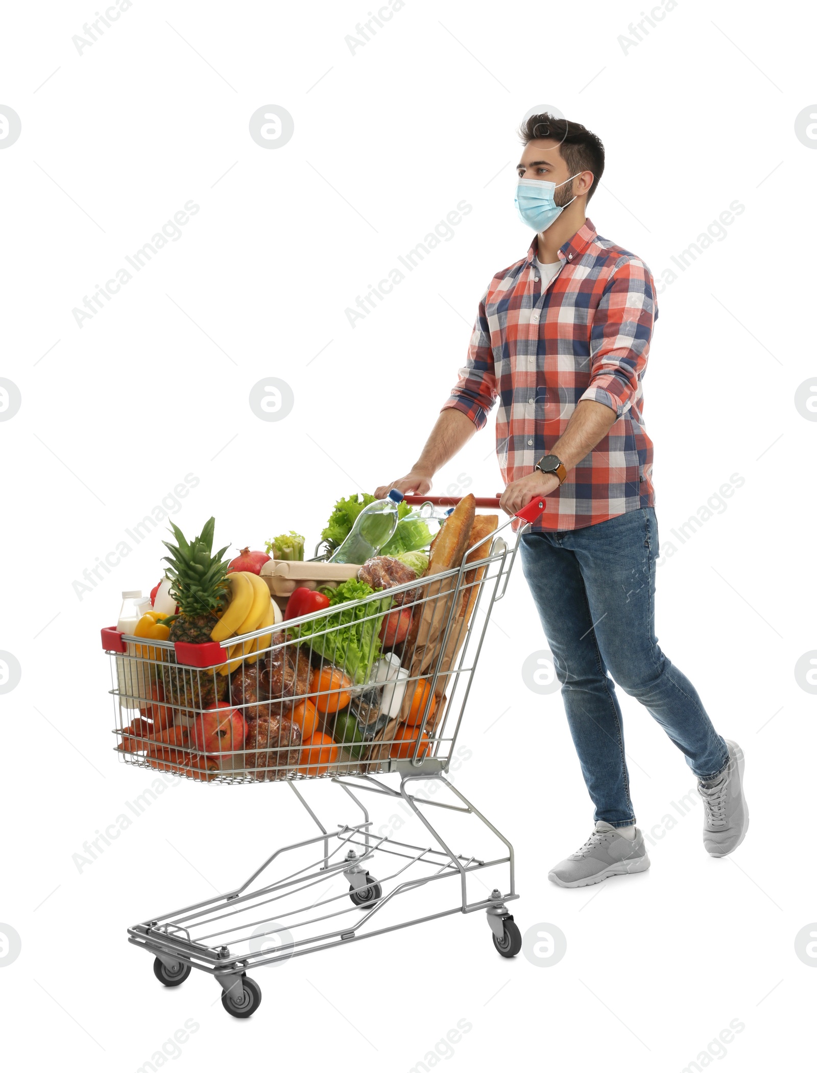 Photo of Young man in medical mask with shopping cart full of groceries on white background